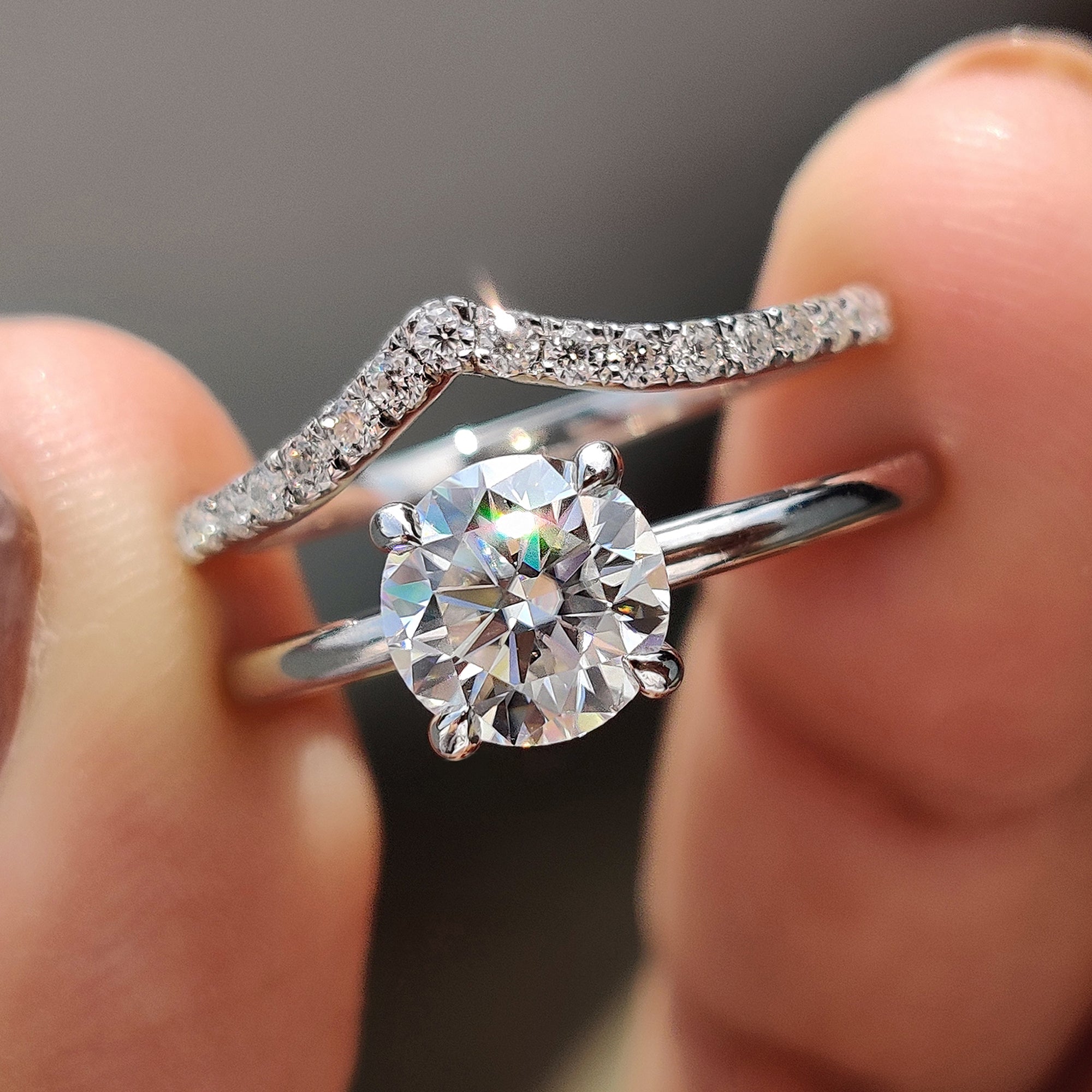 White gold bridal set with a round cut moissanite ring and a curved wedding band.
