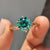 Rose gold solitaire engagement ring with a twisted rope band and green round cut Moissanite in a 6 claw prong setting.
