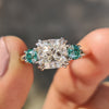 Cushion cut Moissanite engagement ring with green side stones.
