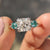 Cushion cut Moissanite engagement ring with green side stones.
