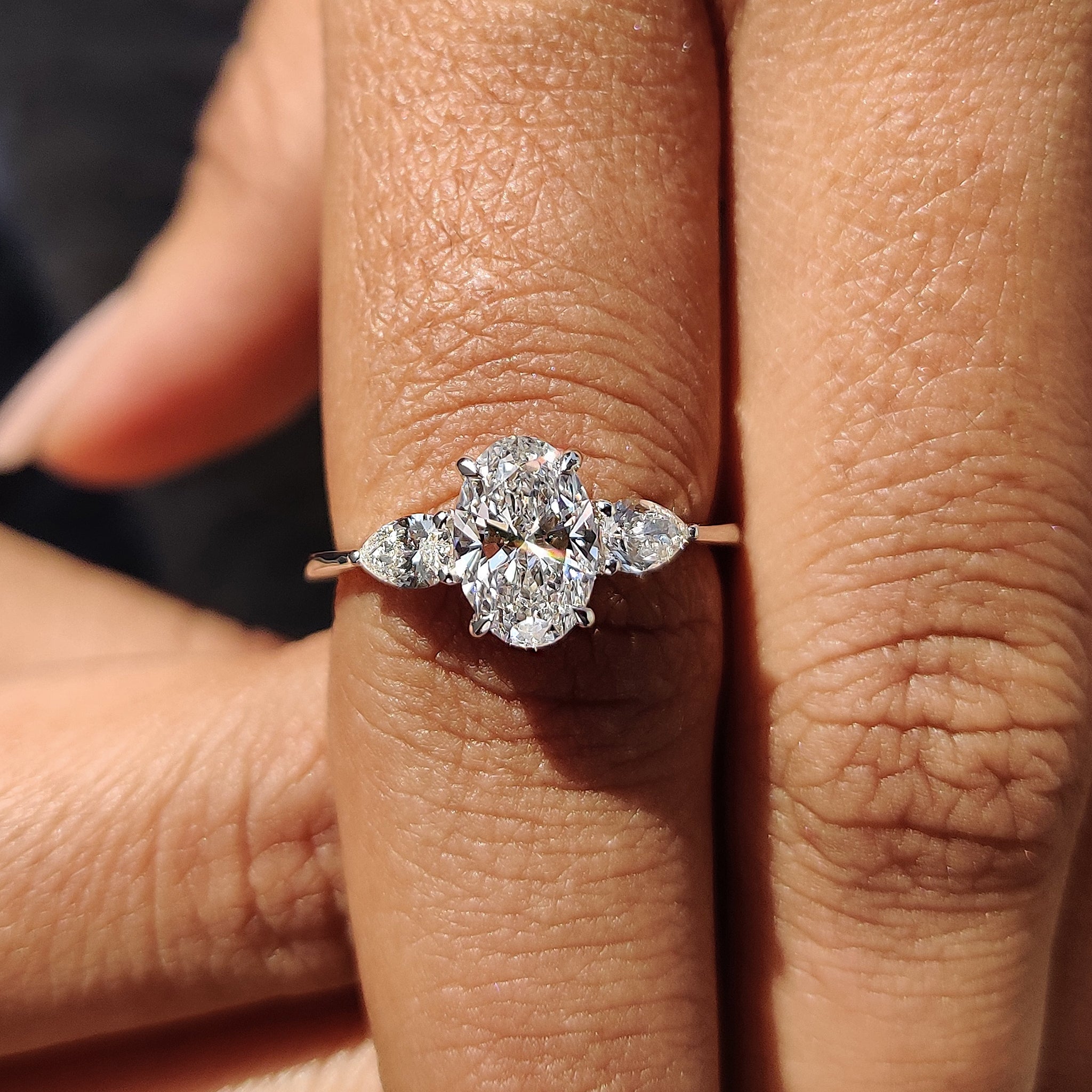 Oval engagement ring with pear side stones and white gold band.
