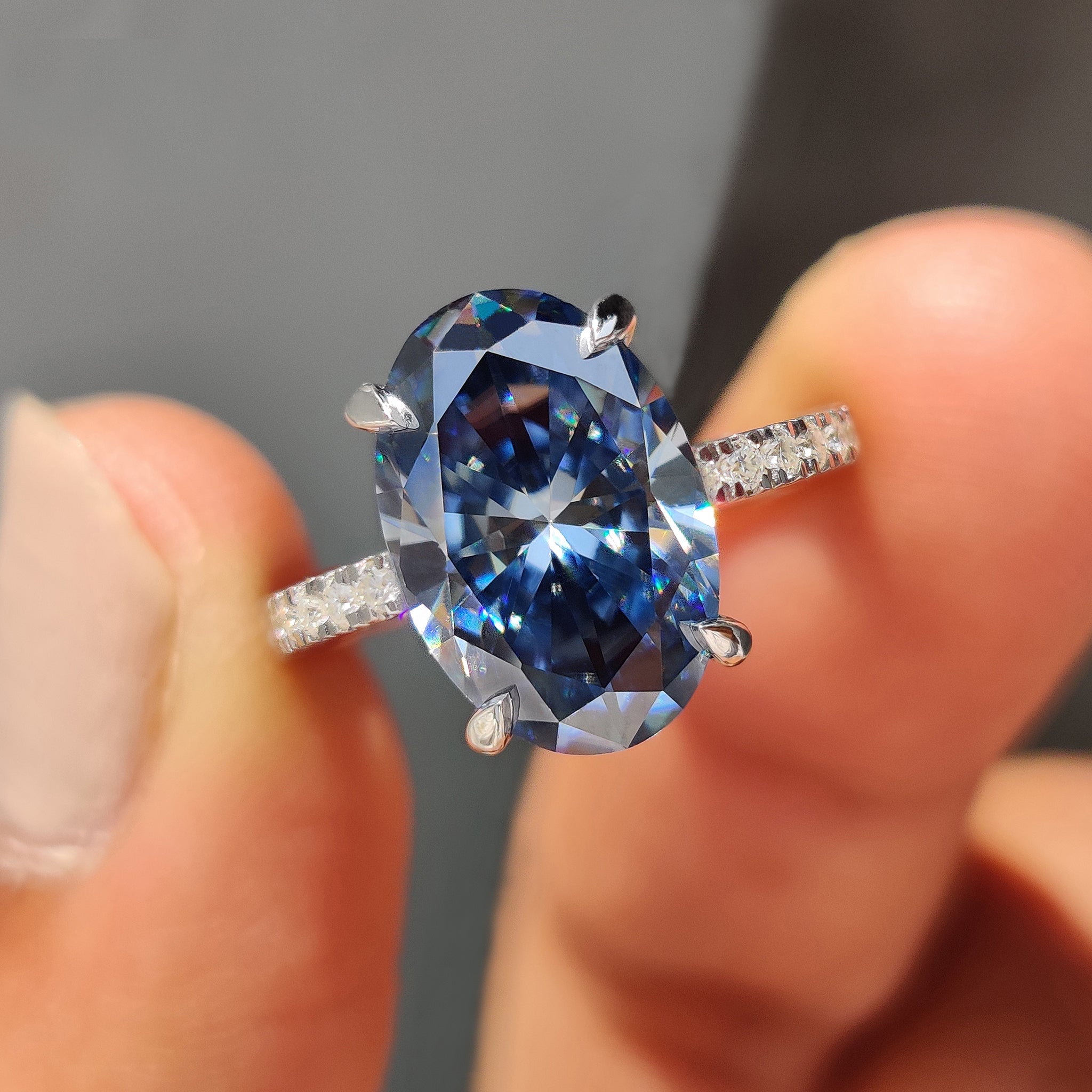 White gold engagement ring with a royal dark blue oval Moissanite in a round cut hidden halo setting.
