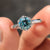 Round engagement ring featuring a hexagon framed setting with a cyan blue round cut Moissanite
