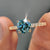 A round cut engagement ring looks stunning with a cyan blue moissanite ring set in a handcrafted finish.
