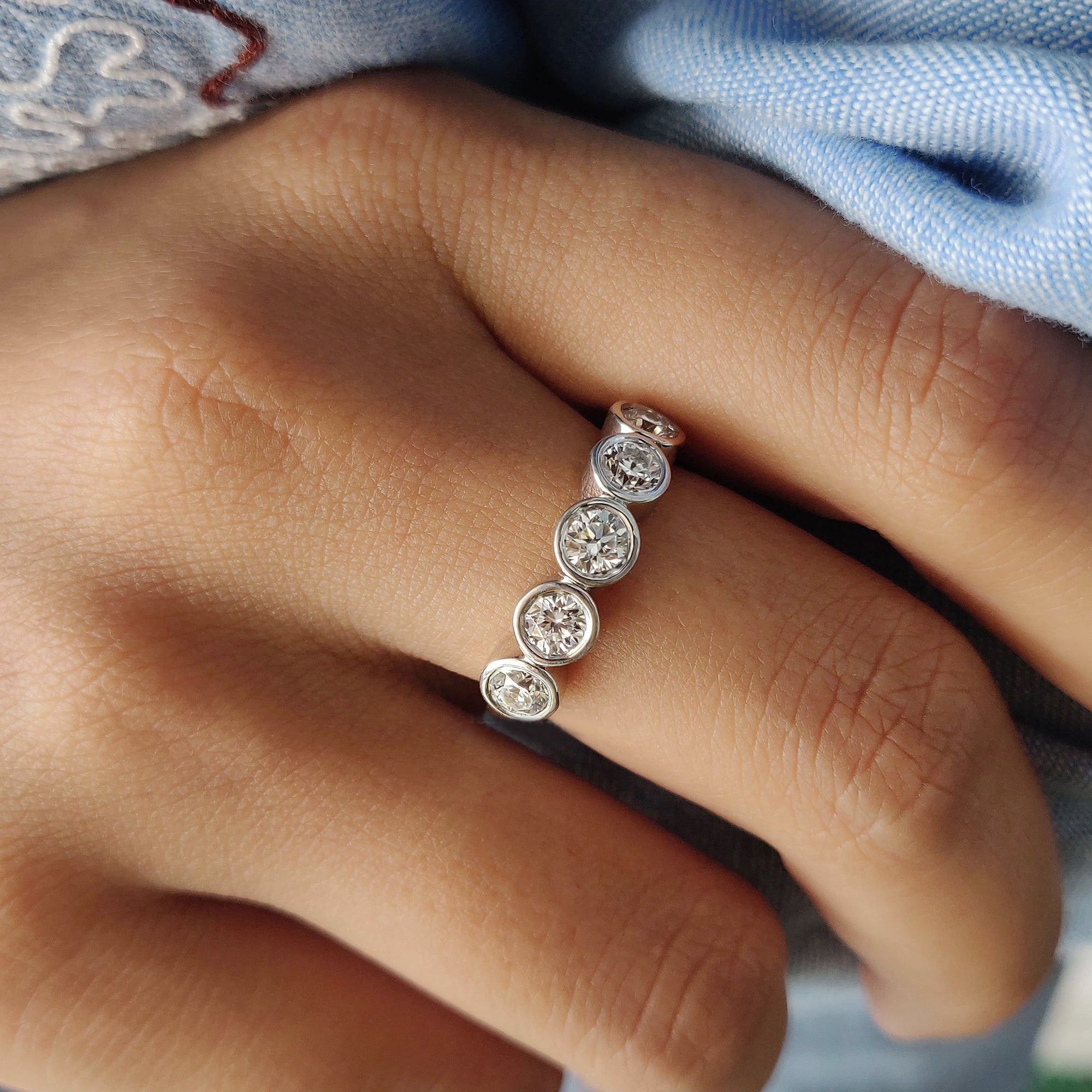 Bezel set round cut moissanite band in white gold.
