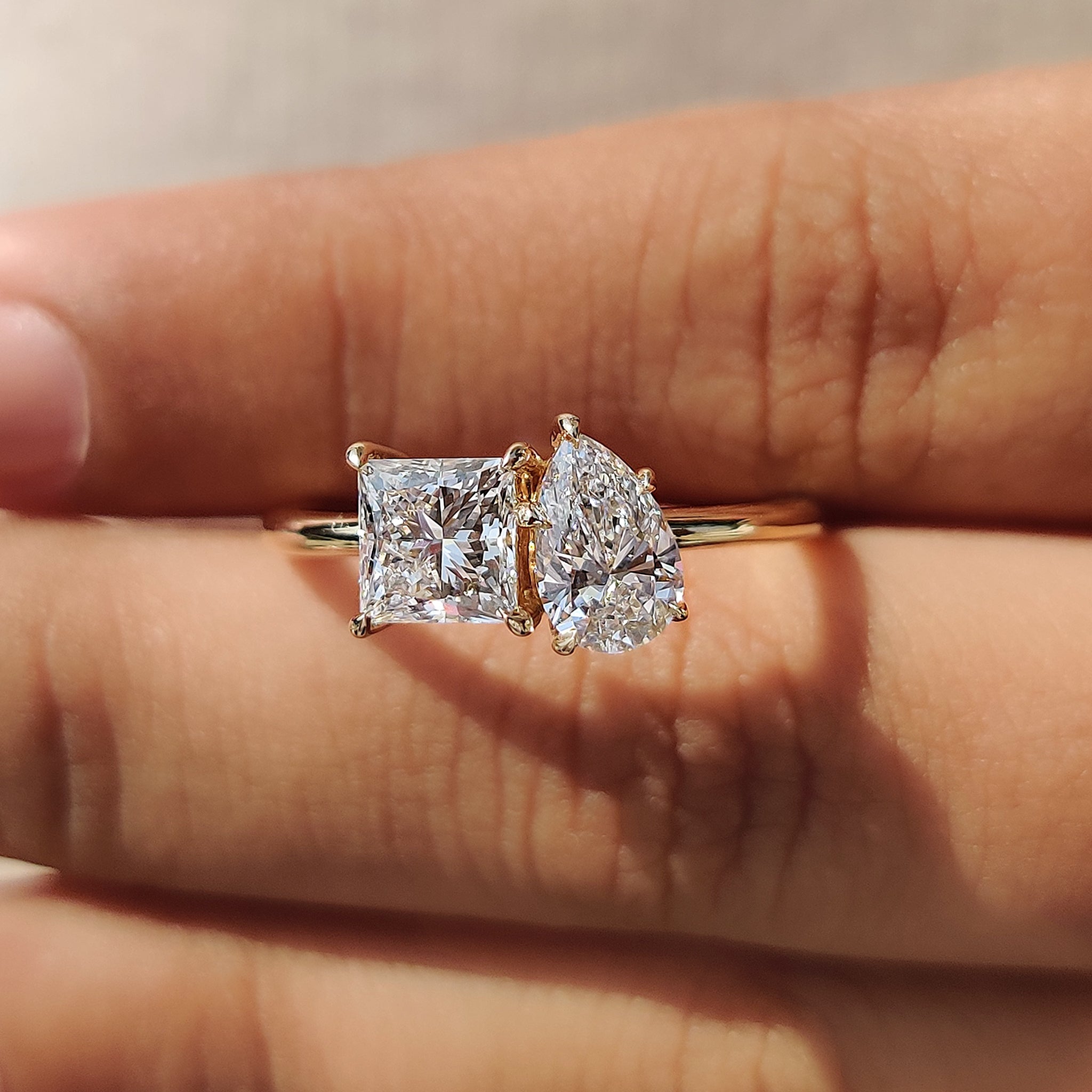 A prong setting 2-stone engagement ring with a princess cut diamond and a pear cut diamond, handcrafted in yellow gold.
