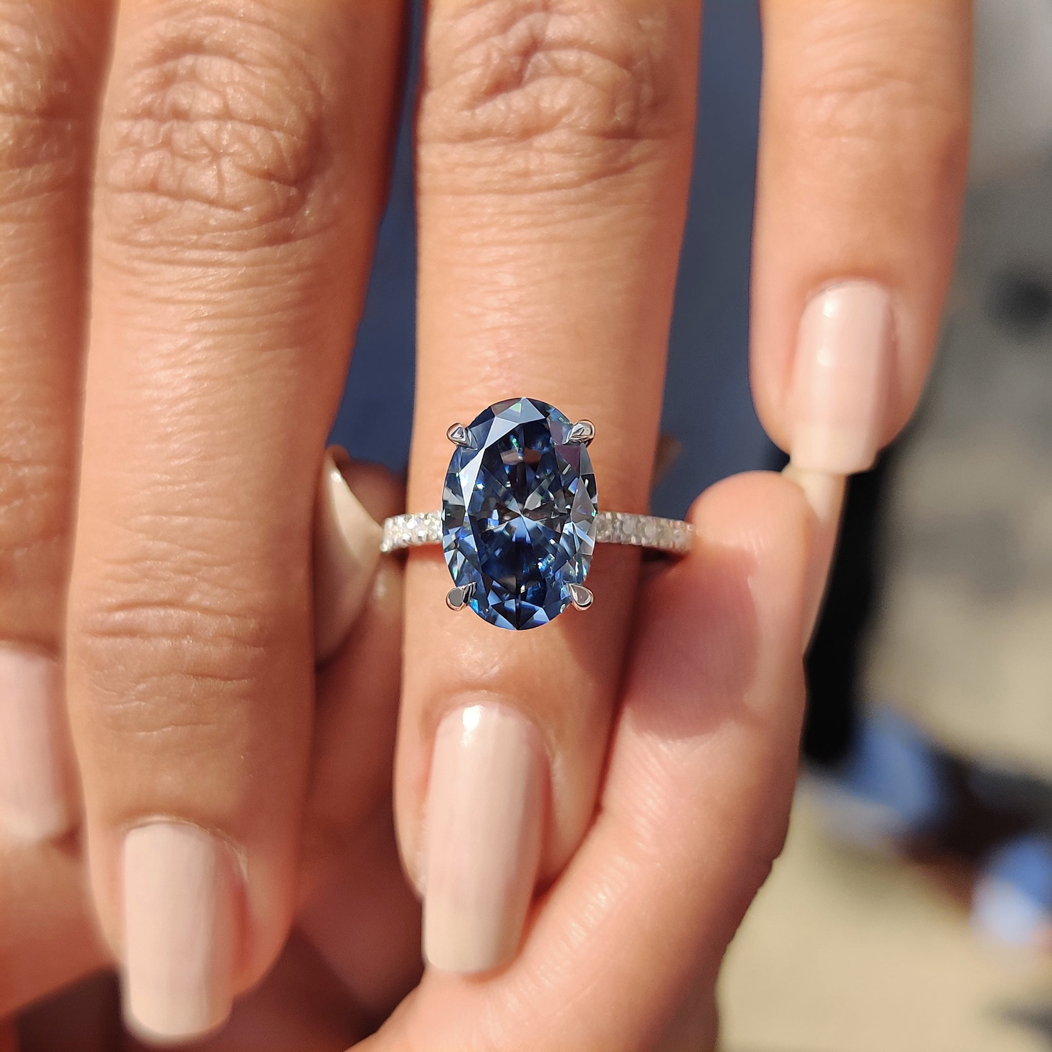 Proposal ring with royal dark blue oval Moissanite in a round cut pave band and 4 claw prong setting.
