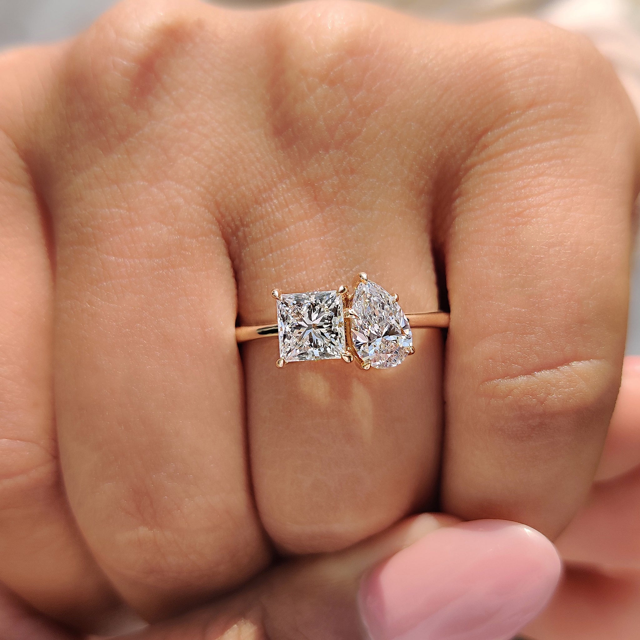 A simple engagement ring with a yellow gold band, featuring a custom design with a pear cut and princess cut diamond.
