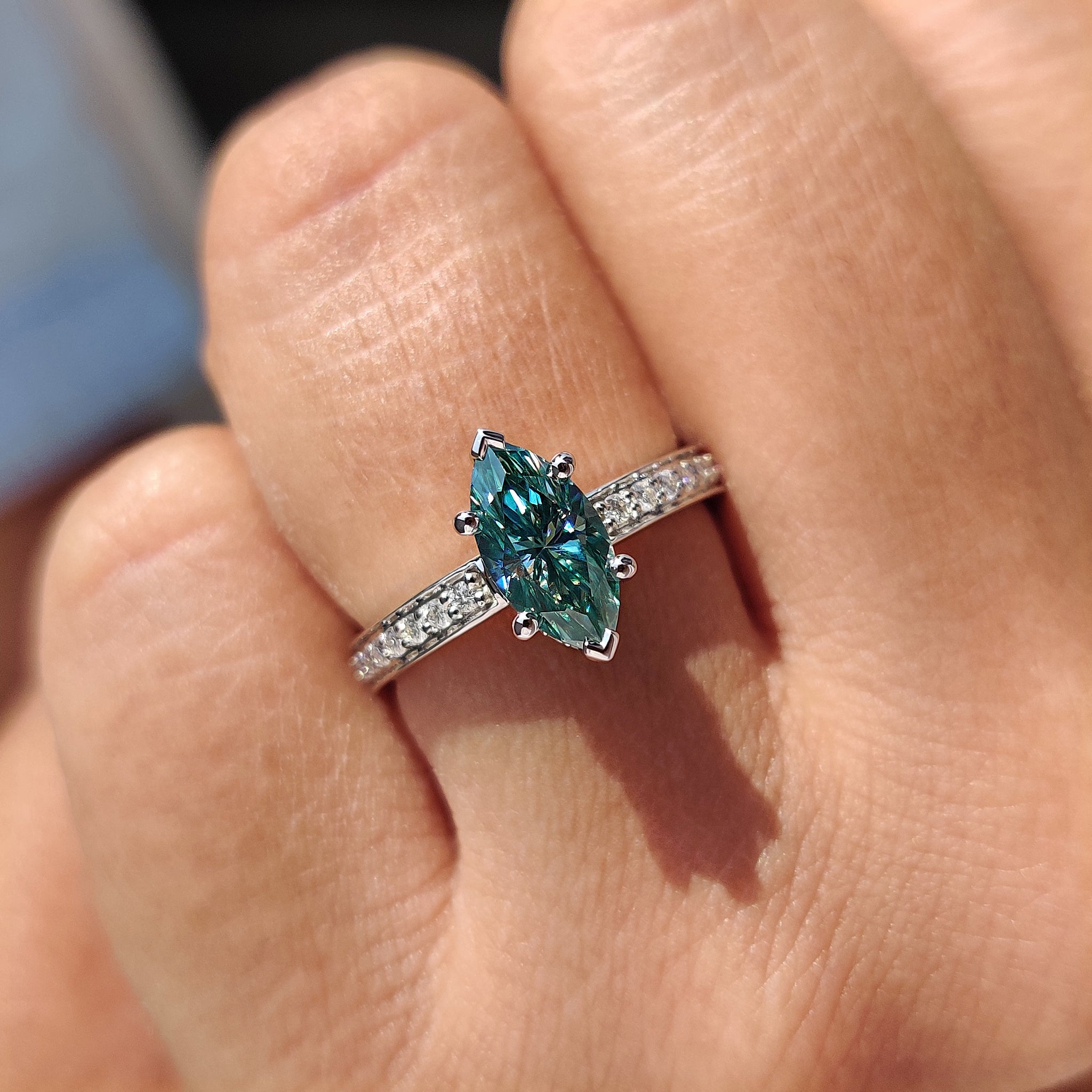 Round cut side stone complementing the marquise moissanite ring design.