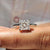 Princess cut solitaire ring in a four claw prong setting with sparkling Moissanite for a modern engagement look.
