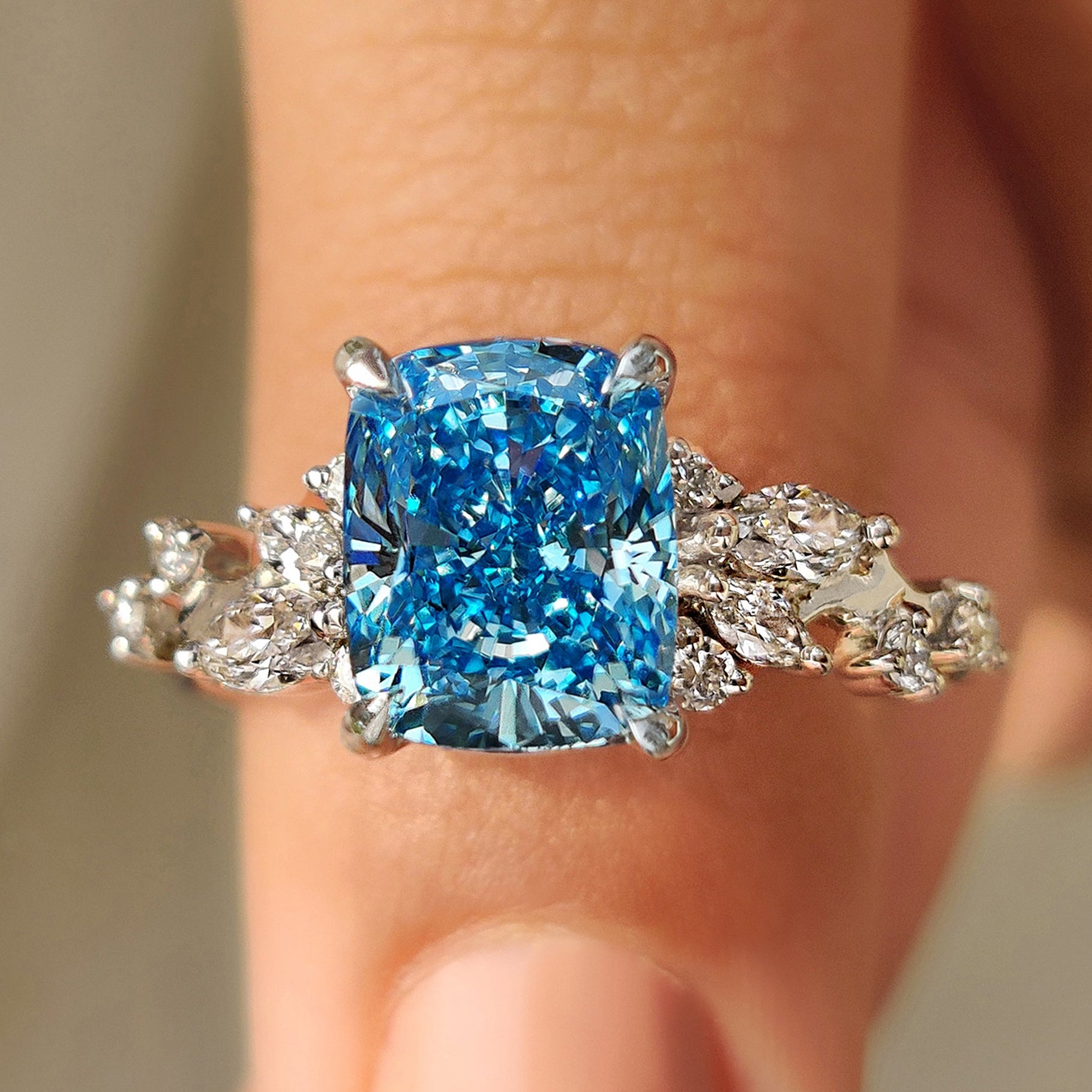 Cushion cut diamond ring with blue diamond cluster setting and side stones.
