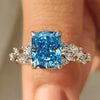 Cushion cut diamond ring with blue diamond cluster setting and side stones.
