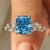 Cushion cut diamond ring with blue diamond cluster setting and side stones.
