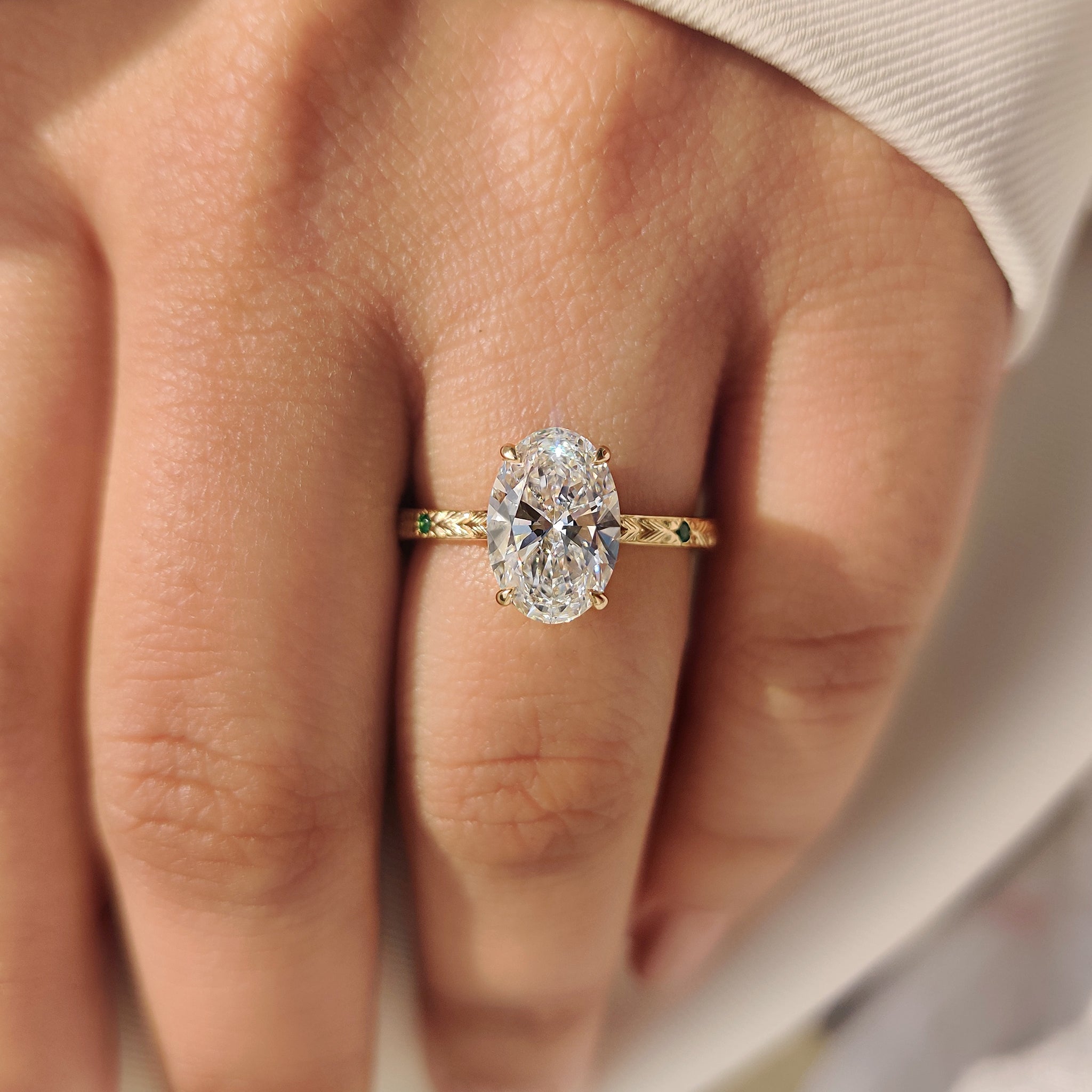 Oval diamond ring with round cut emerald side gemstones.
