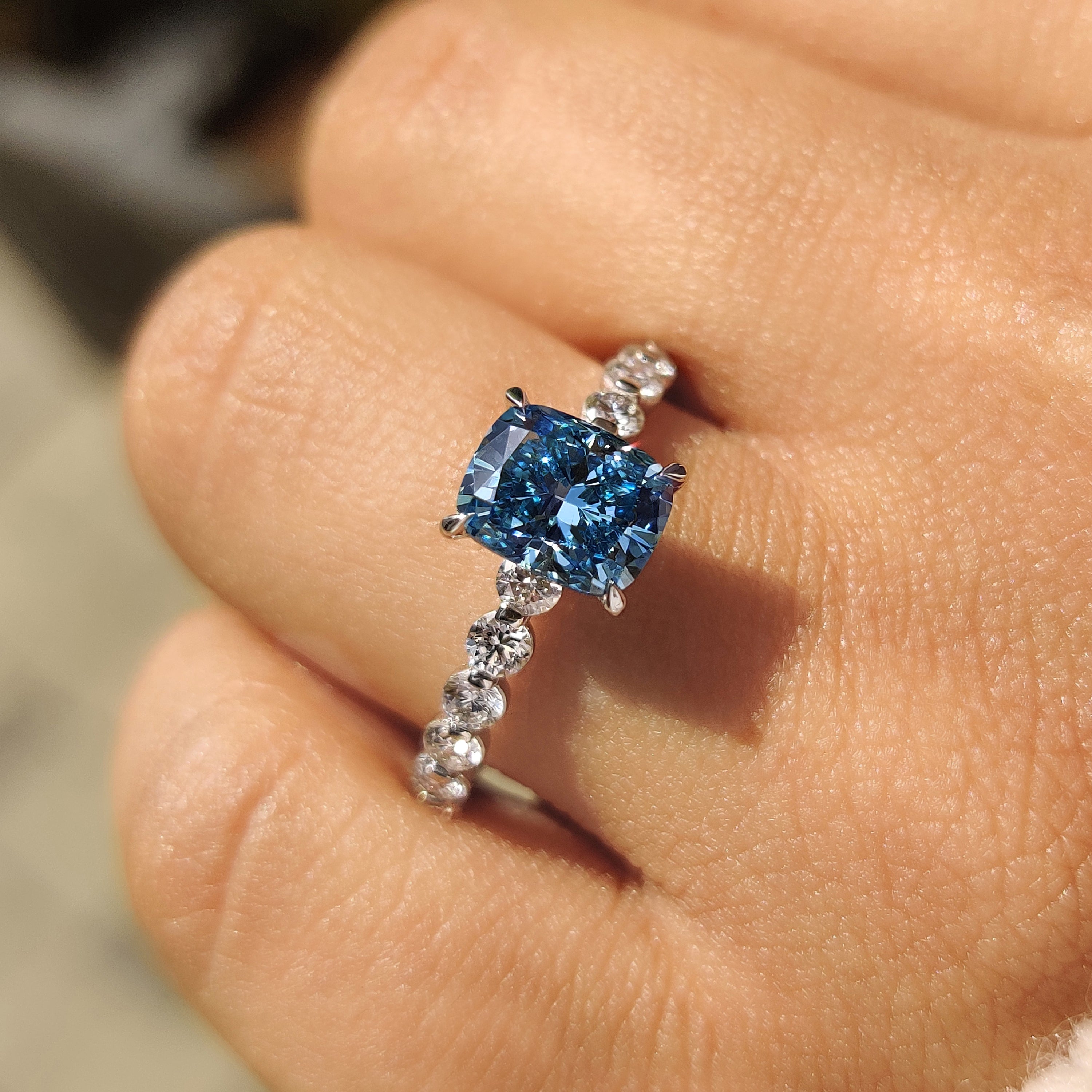 Blue cushion ring with round diamond accents.
