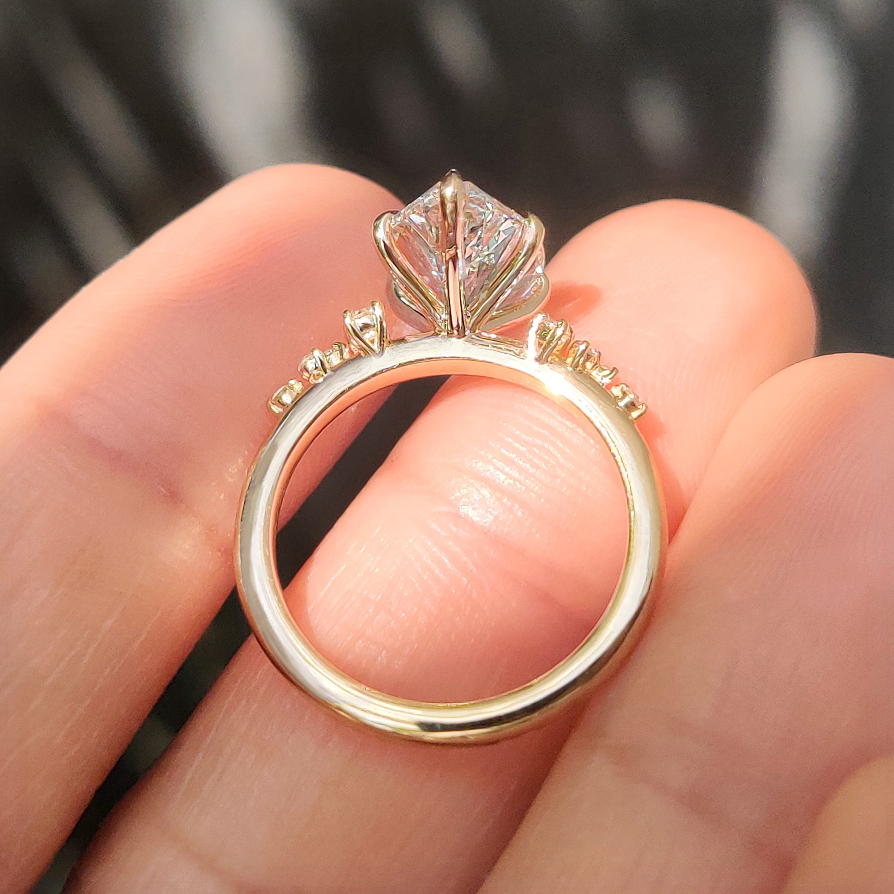 Cluster setting enhances marquise cut engagement ring with round side stones.
