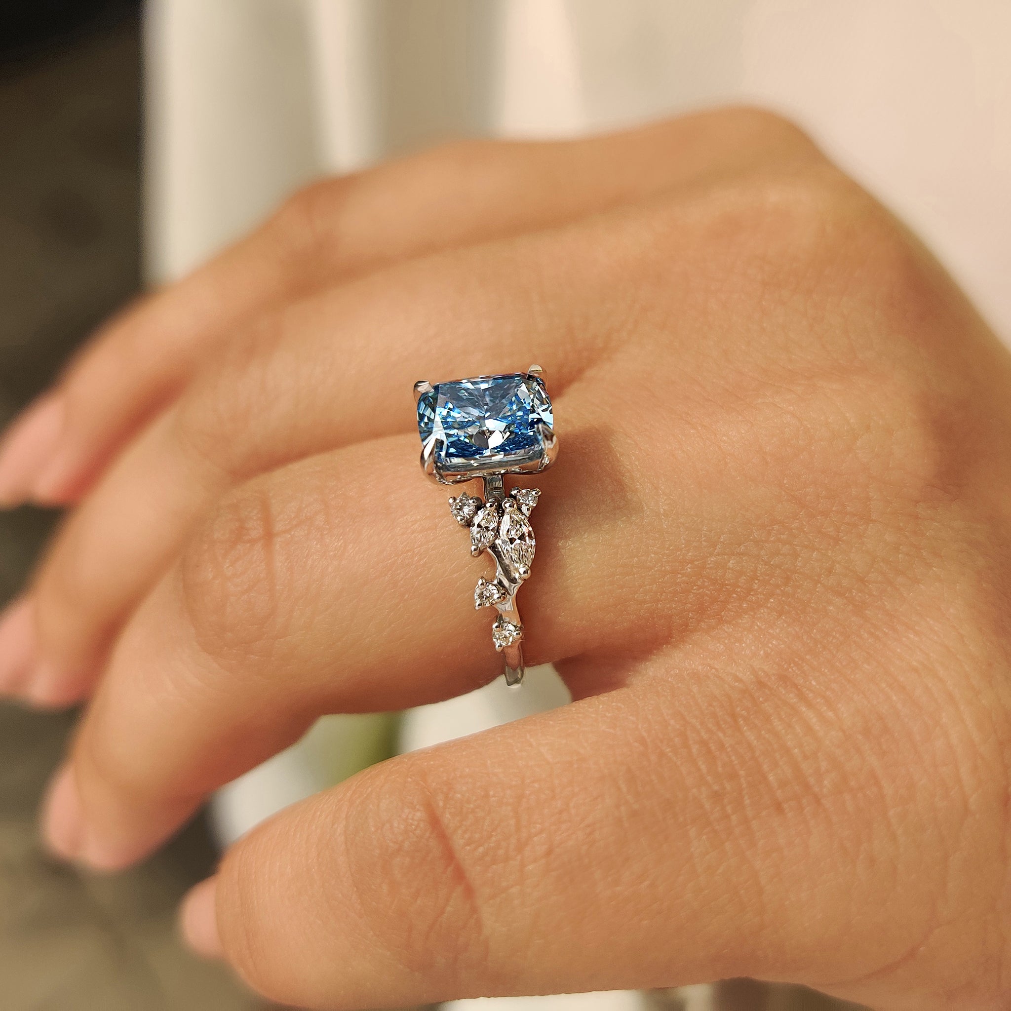 Cushion cut blue diamond ring in cluster setting with four claw prongs.
