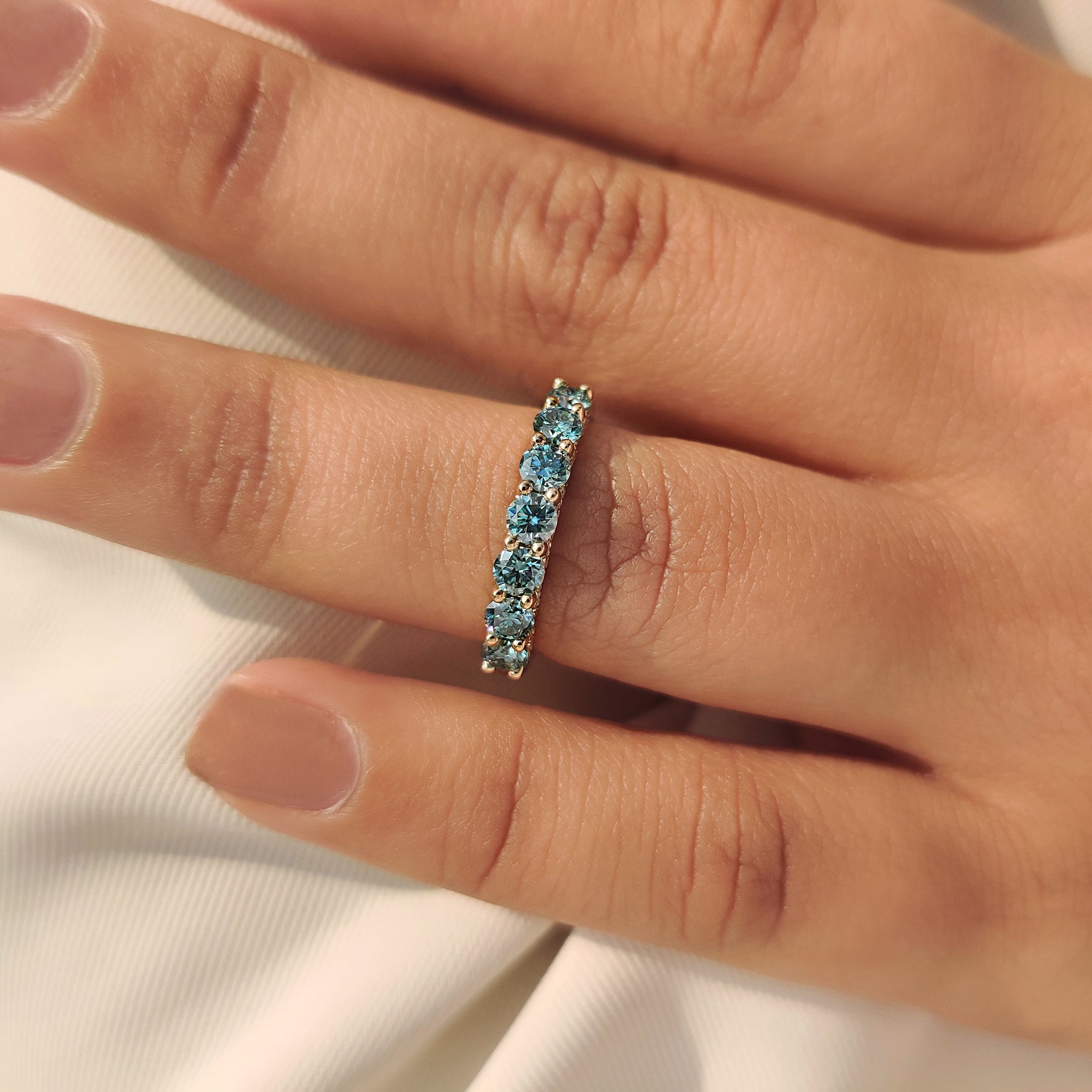 Seven stone blue moissanite band with shared prong style.
