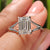 Elegant emerald cut diamond solitaire ring with a split shank design, showcasing a lab-grown diamond in a white gold setting.
