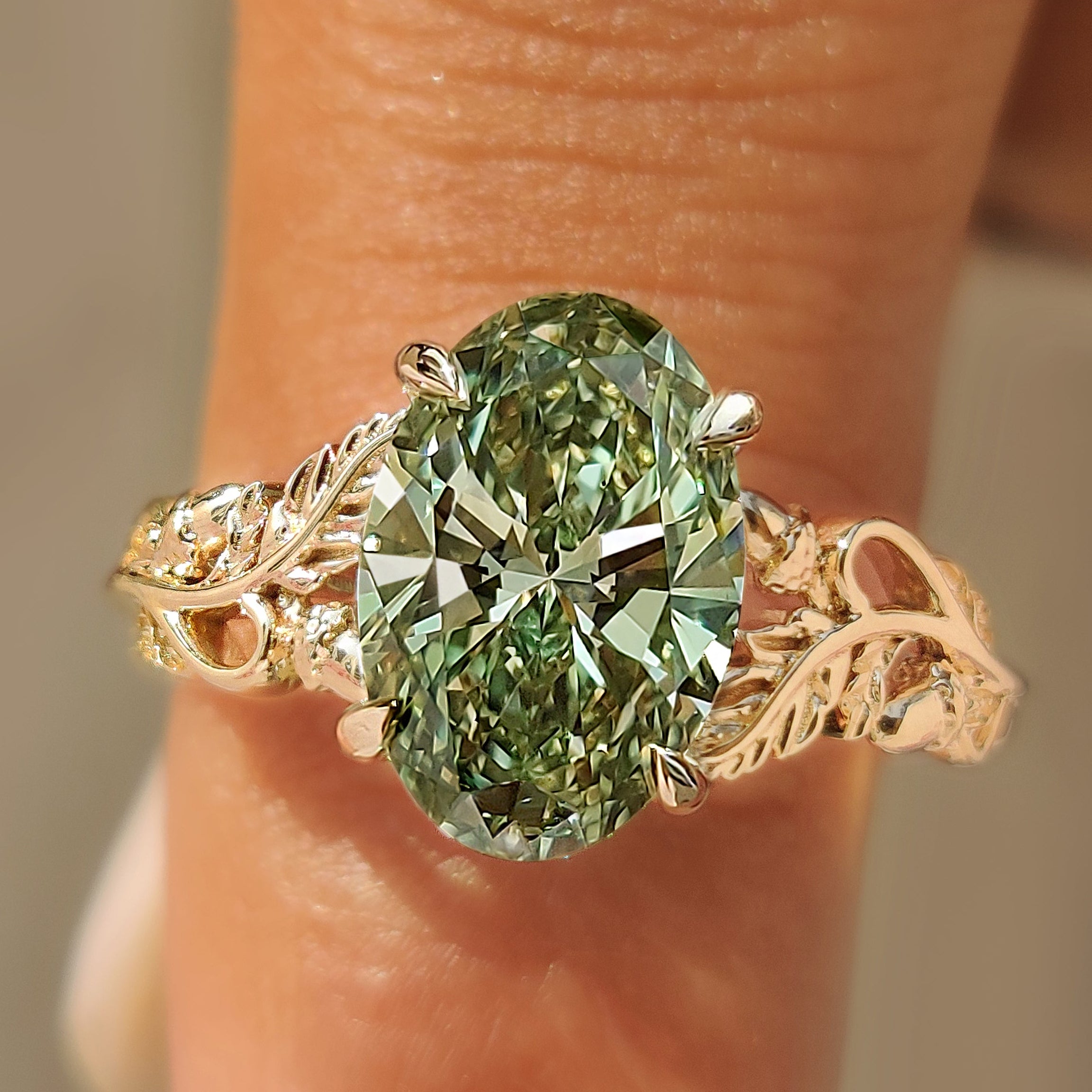 Green oval cut diamond solitaire ring with leaf and vine detailing.
