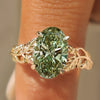 Green oval cut diamond solitaire ring with leaf and vine detailing.
