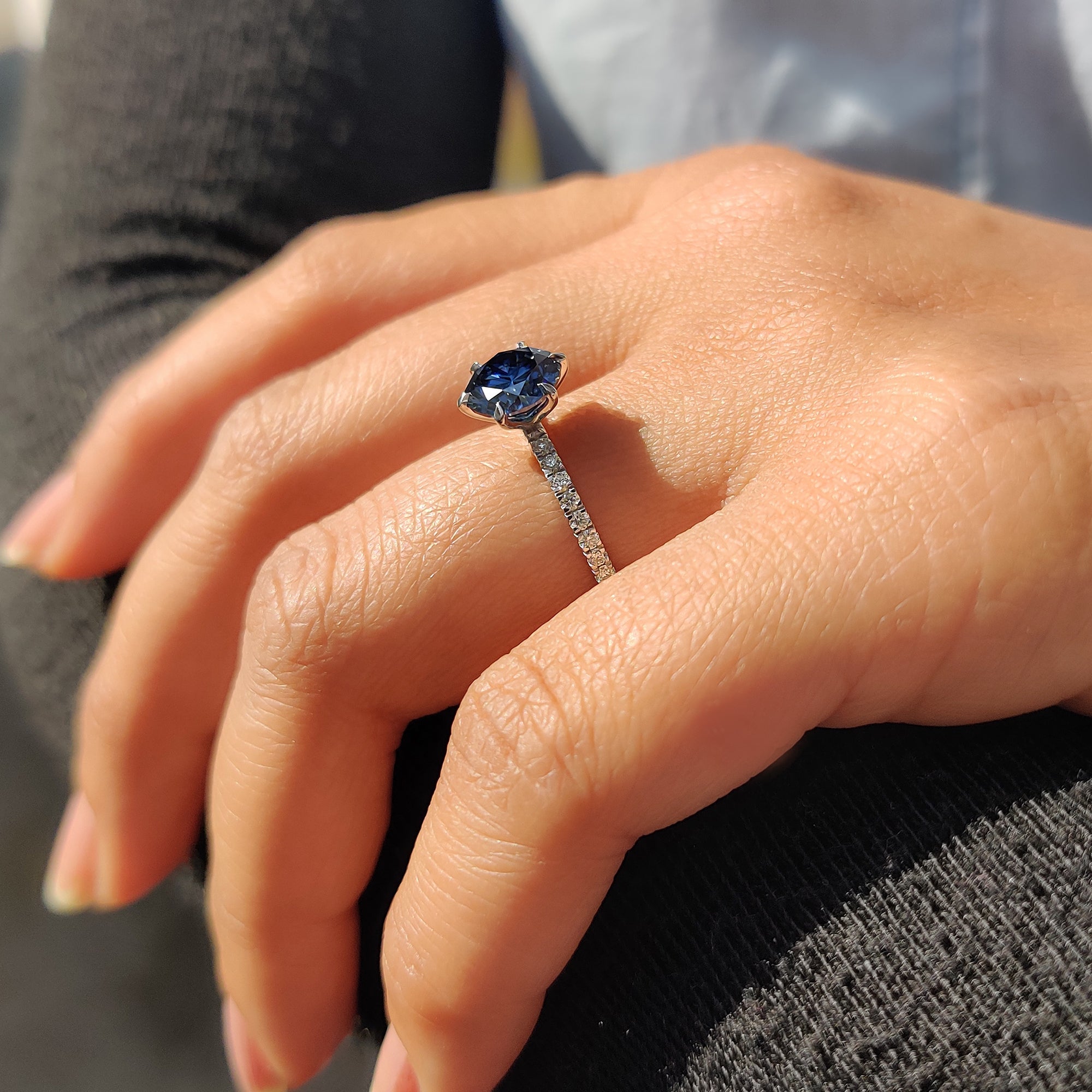 Proposal ring with round pave band and royal dark blue round cut Moissanite in a 6 claw prong setting.
