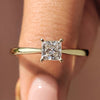 Elegant tapered ring shank design holds a princess cut solitaire diamond in a yellow gold setting.