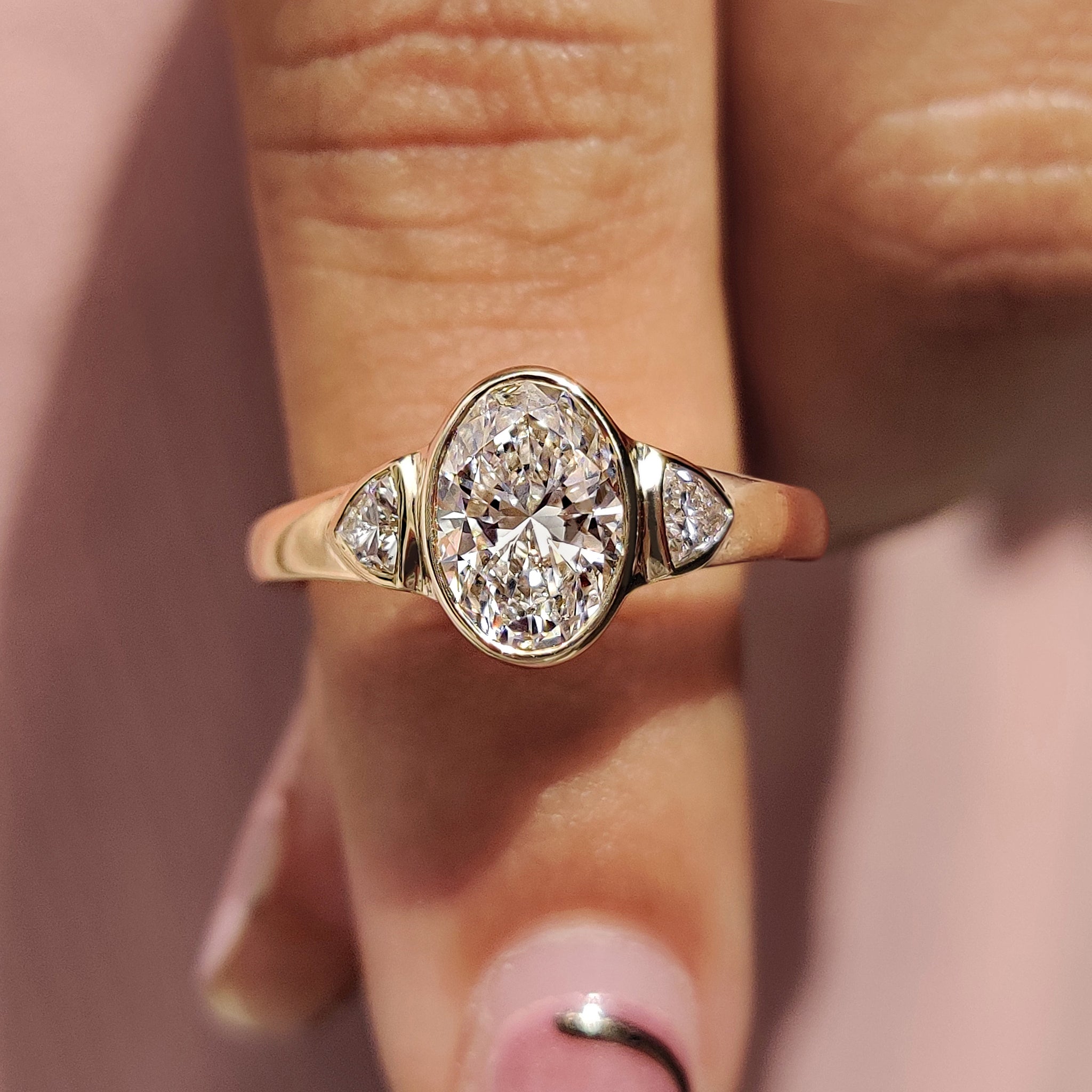 Oval bezel engagement ring with trillion side stone.
