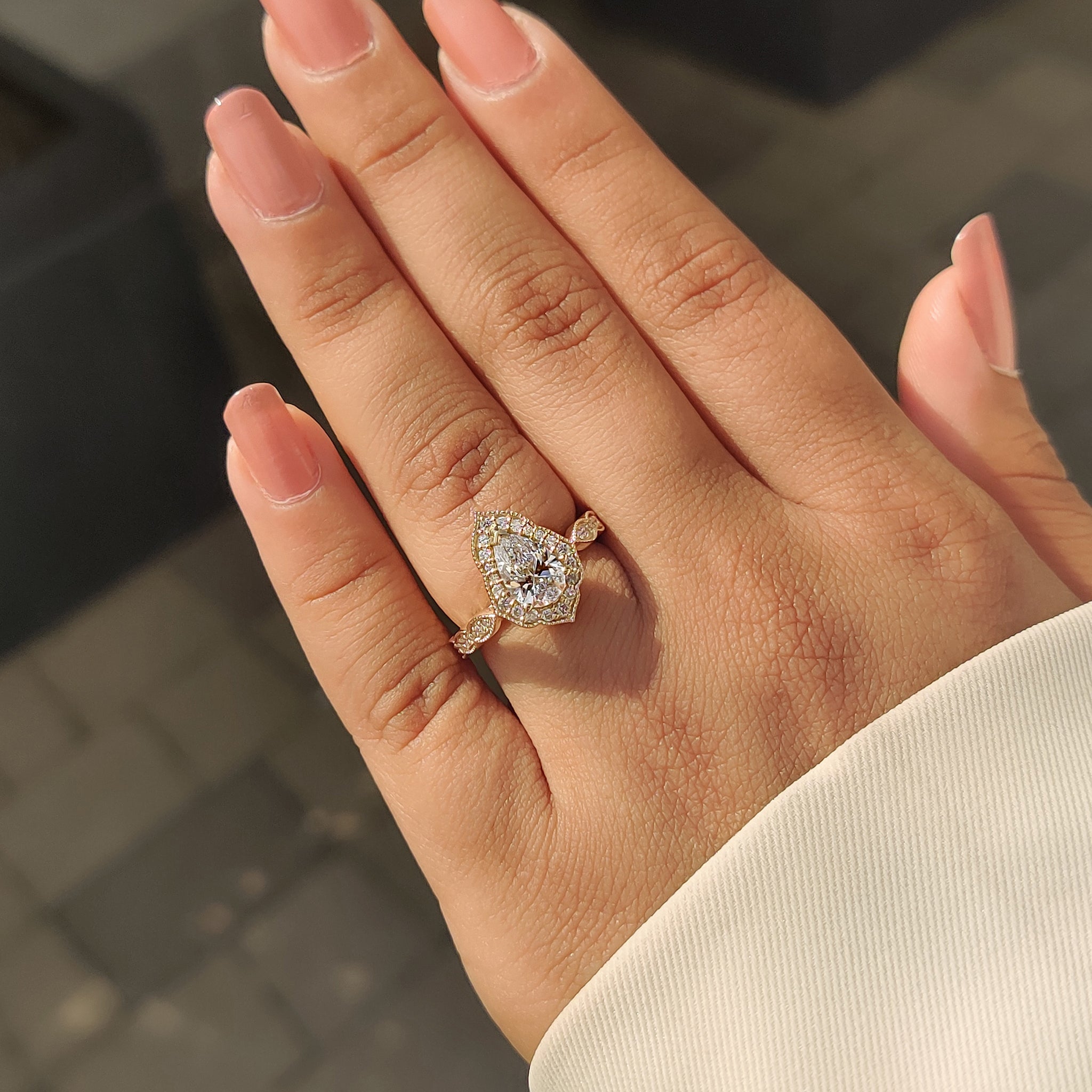 Yellow gold engagement ring with pear cut diamond, milgrain details, and halo setting.