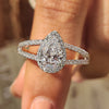 Split shank diamond ring with pear cut center diamond and round cut side stones in white gold.
