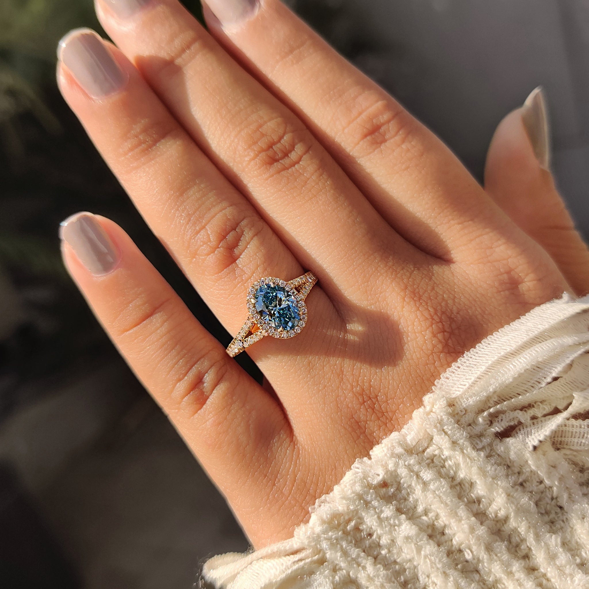 Four claw prong oval engagement ring with blue diamond.