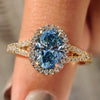 Oval engagement ring with blue diamond and round cut halo.
