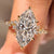Marquise cut engagement ring sparkles with cluster setting and round stones.
