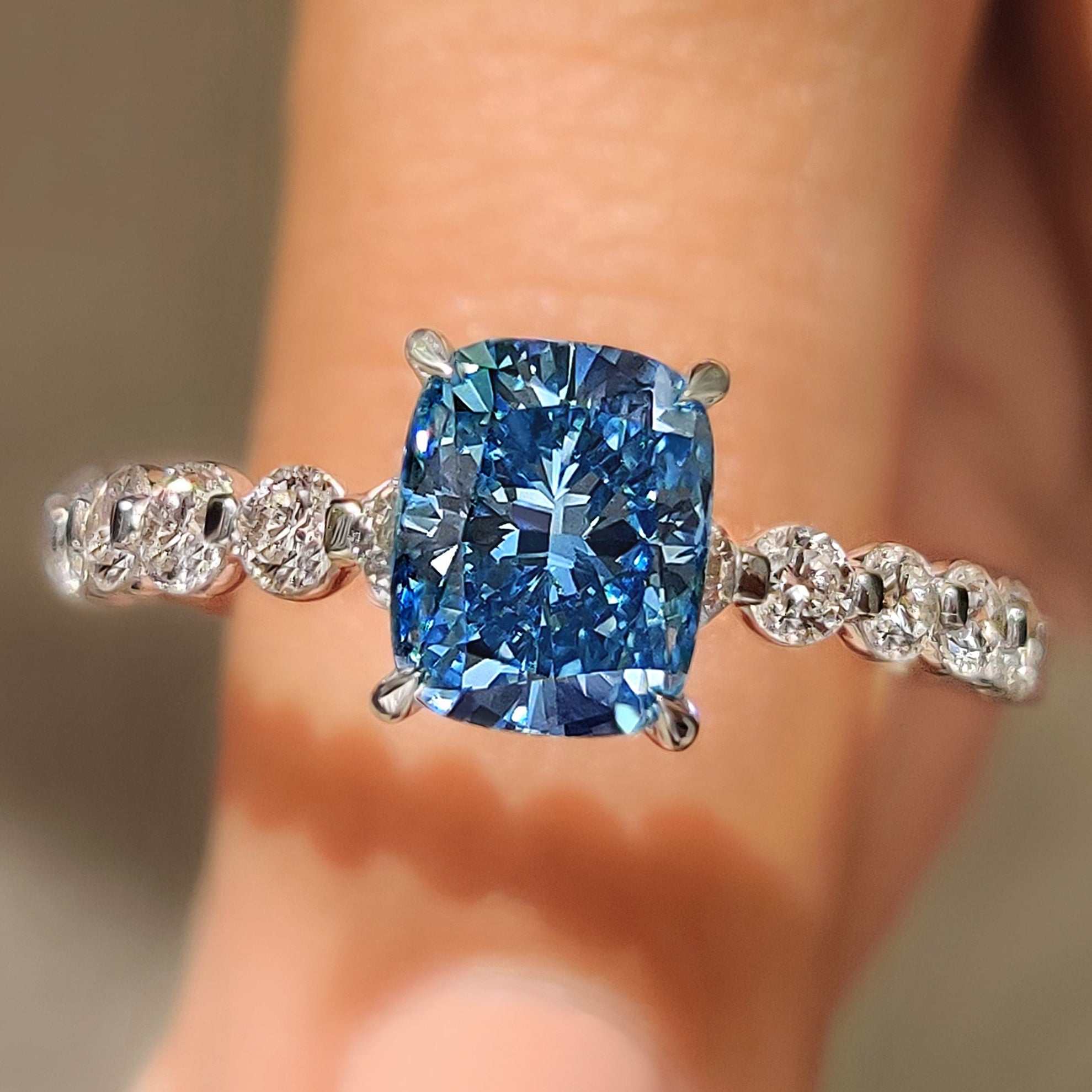 Cushion cut blue diamond ring with pave band.
