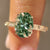 Green oval center diamond with round diamond accents.
