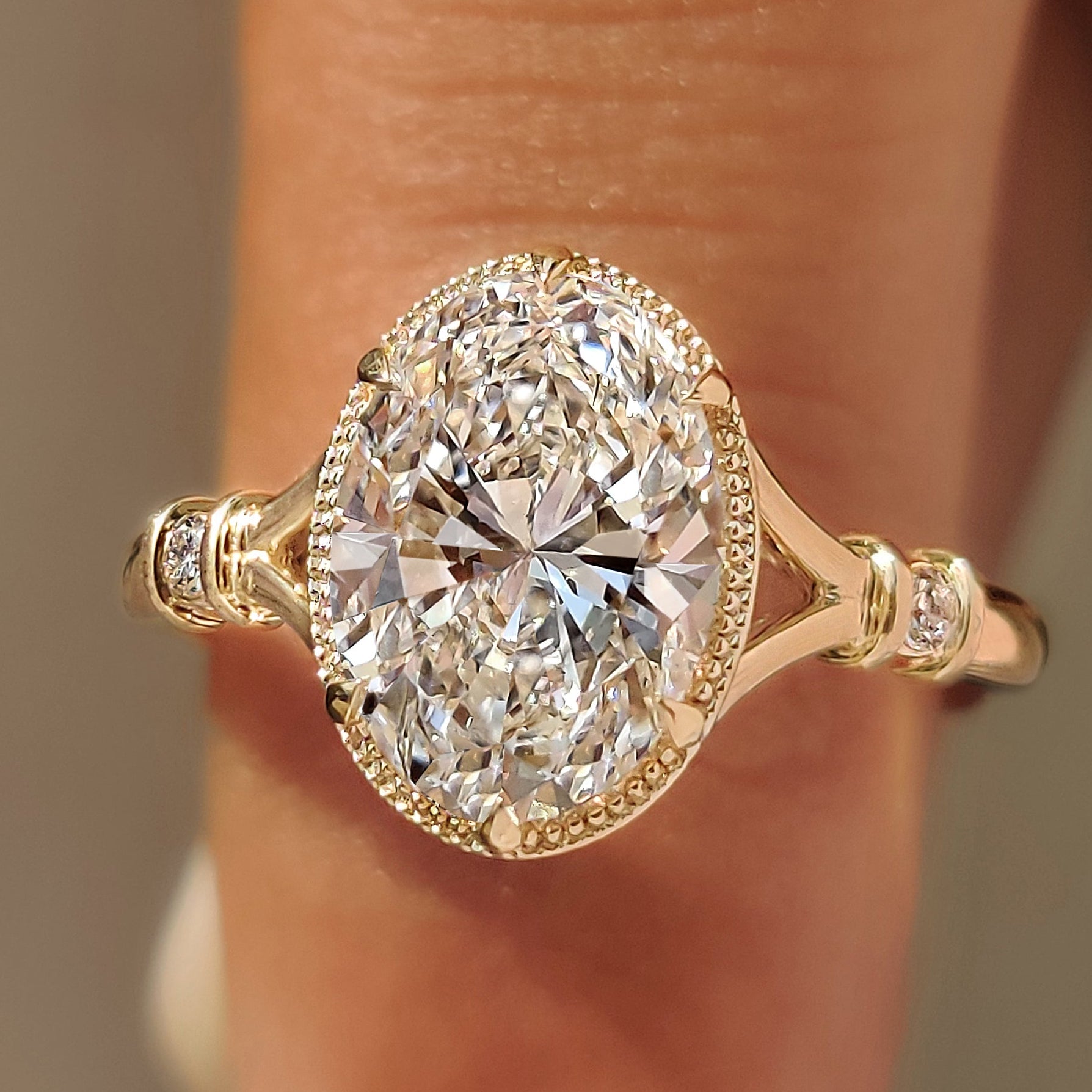 Oval center diamond bezel engagement ring with round side stones.
