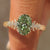Green oval cluster ring with floral engraved band.
