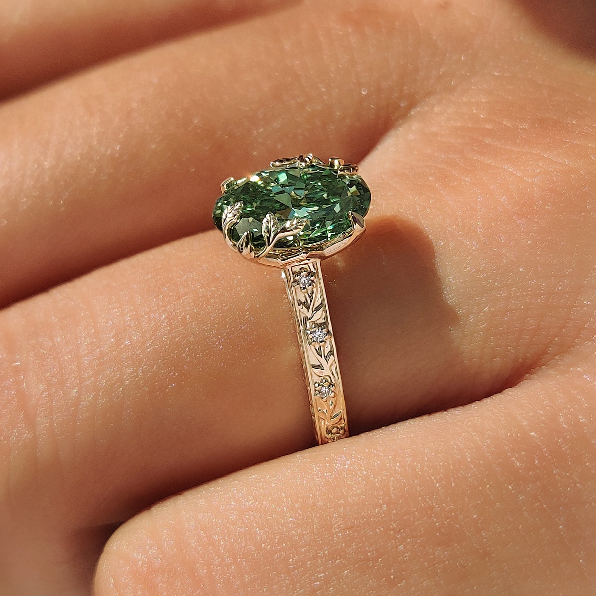 Leaf detailing on a green oval cut center diamond.
