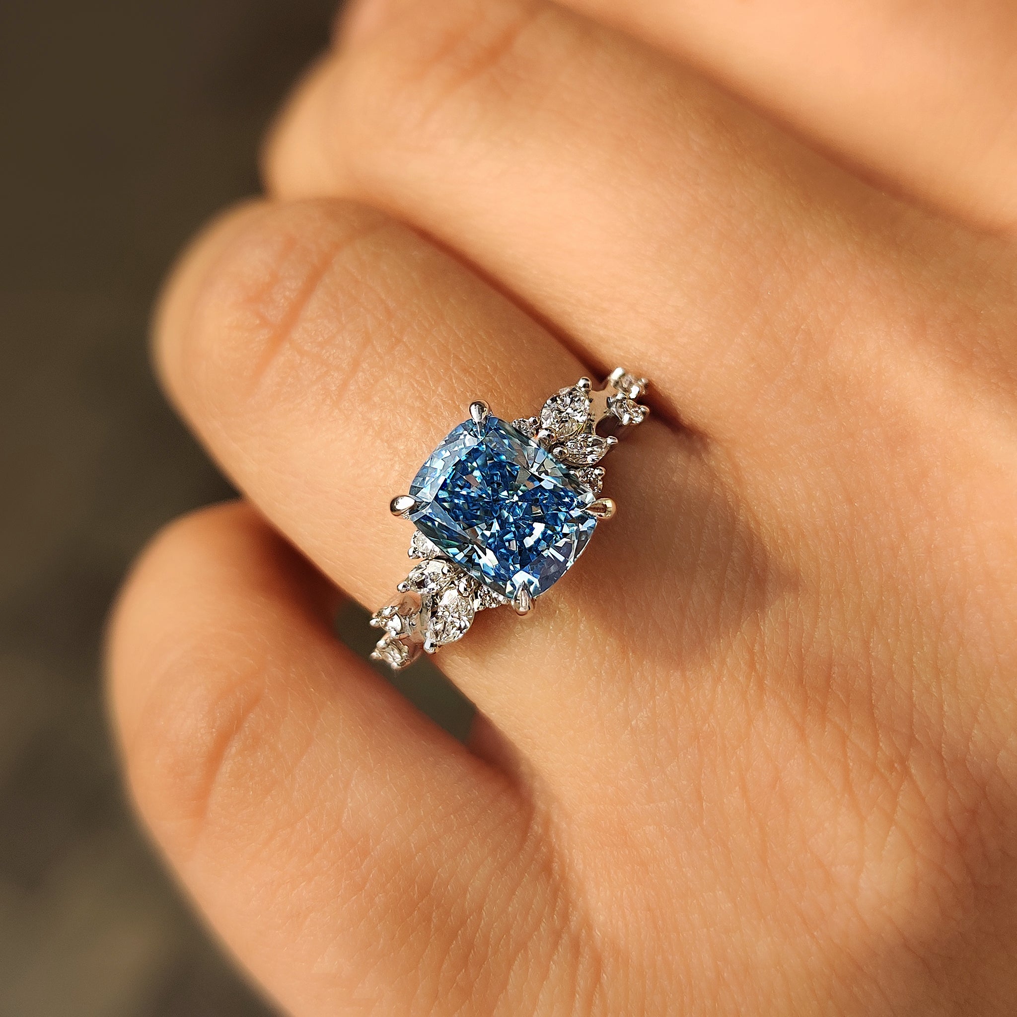 Cushion cut diamond ring featuring blue stone and cluster design.
