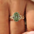 Green oval center diamond held by four claw prongs.
