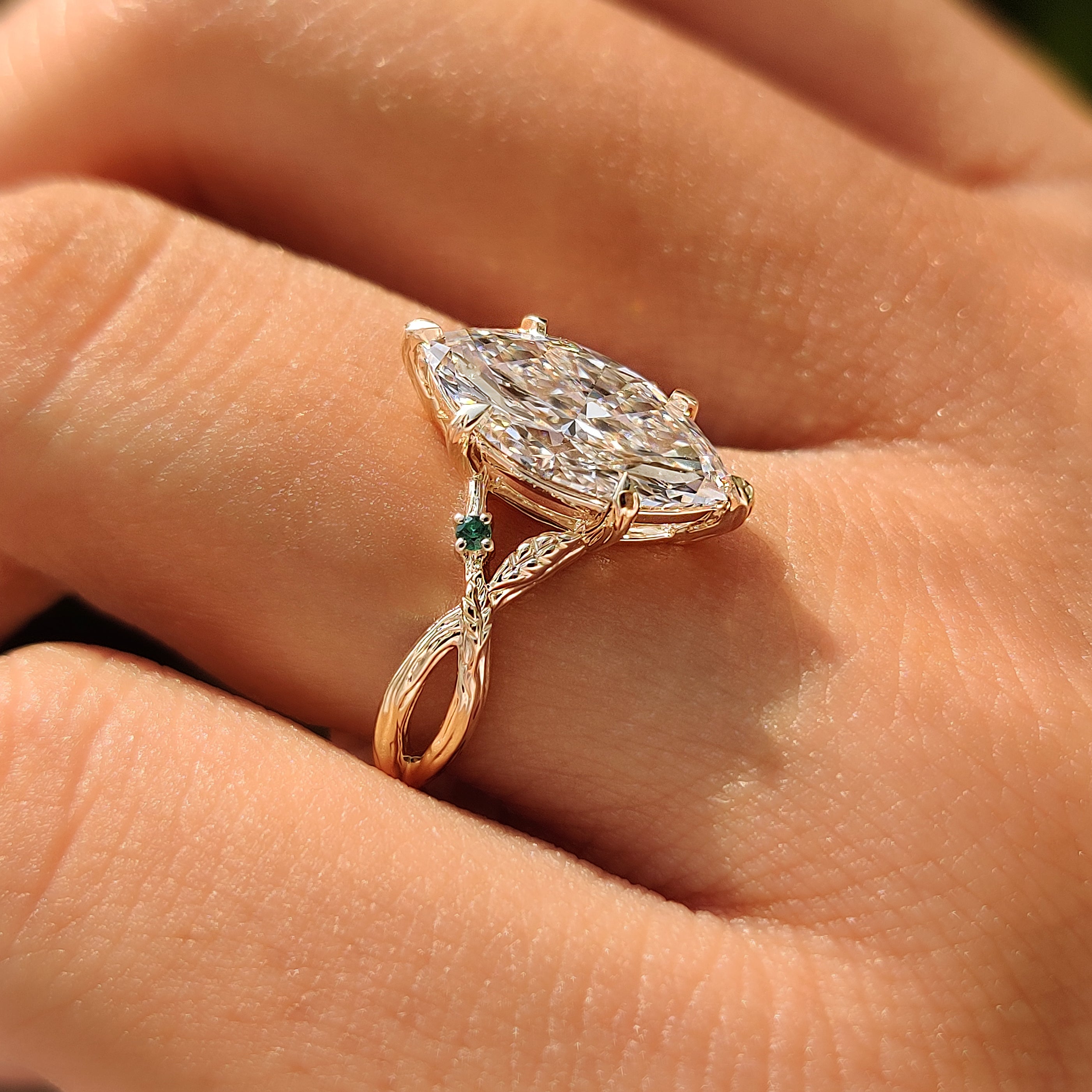 Green emerald gemstone accents beside a marquise diamond.

