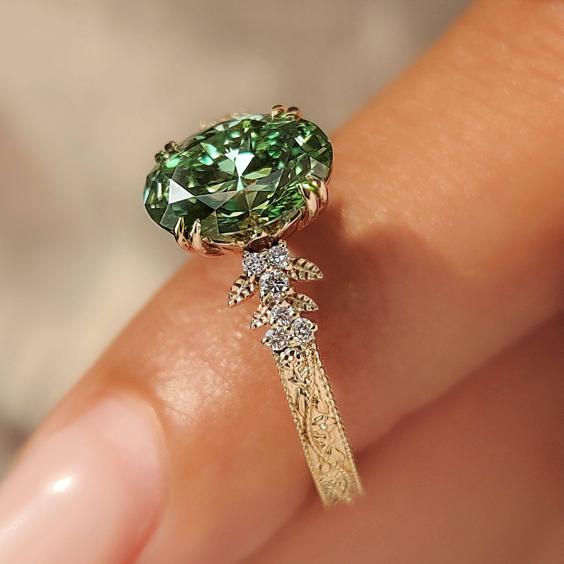 Double claw prongs holding a green oval diamond.
