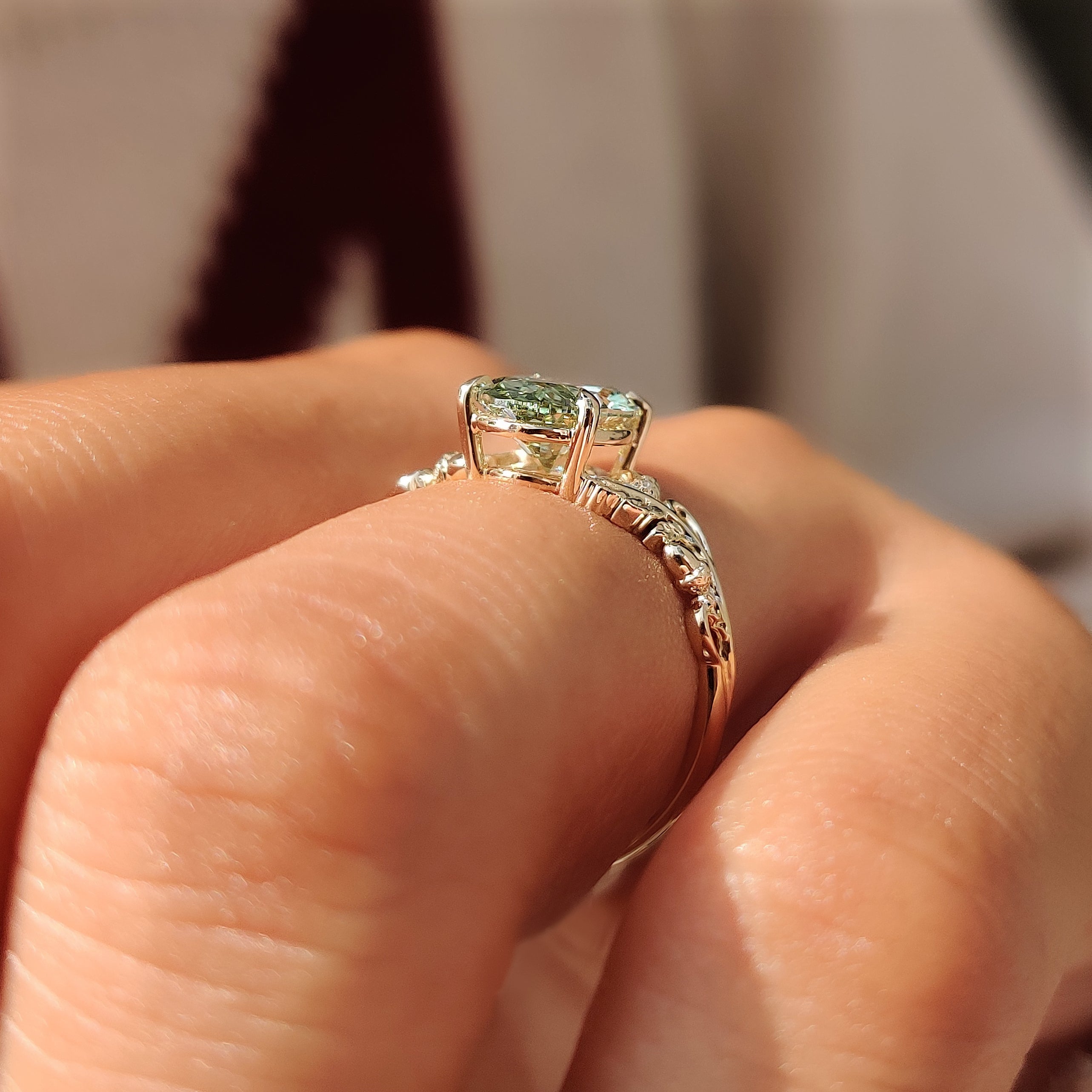 Green oval solitaire ring with decorative vine shoulders.
