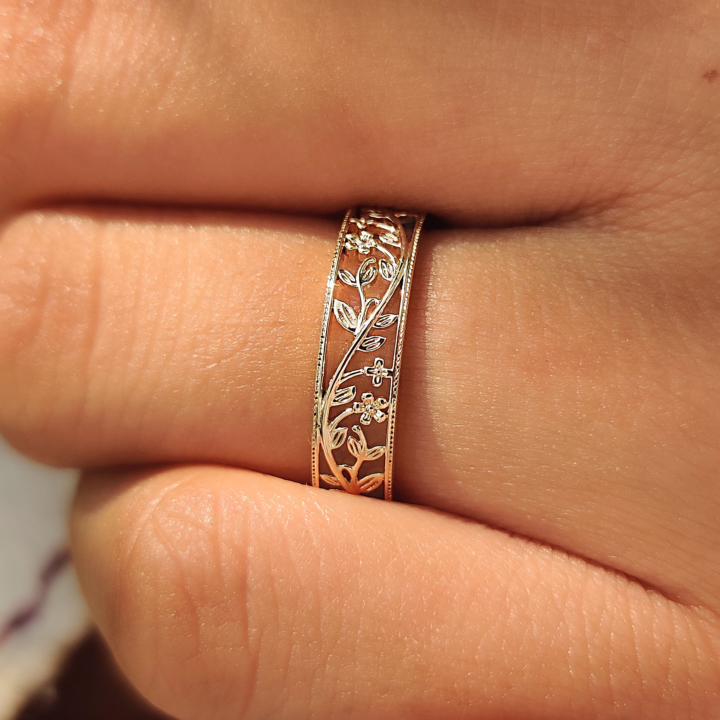 Openwork flower wedding band shown on a finger.

