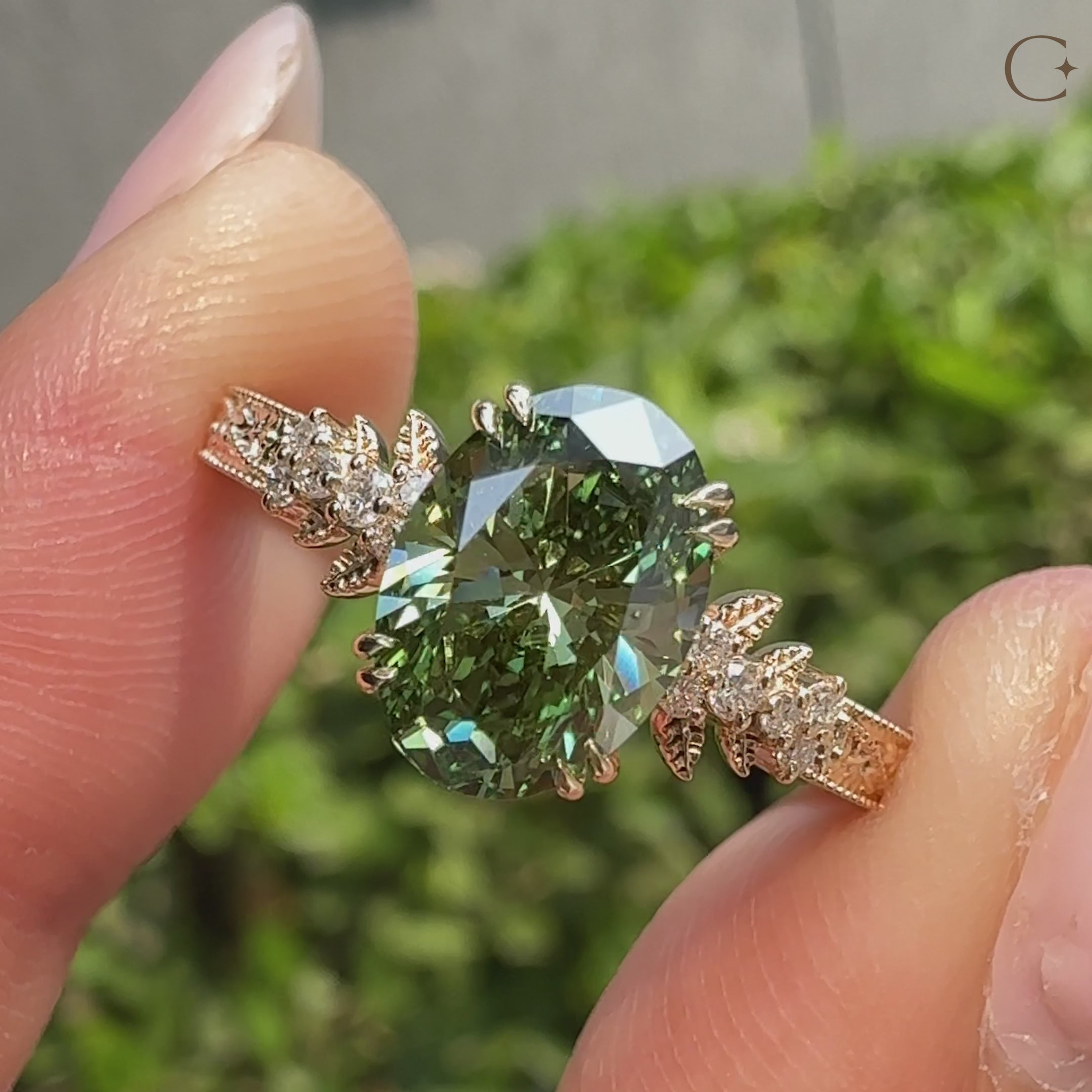 Cluster engagement ring with green oval center and round accent diamonds.
