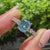 Blue cushion diamond ring with round pave stones.